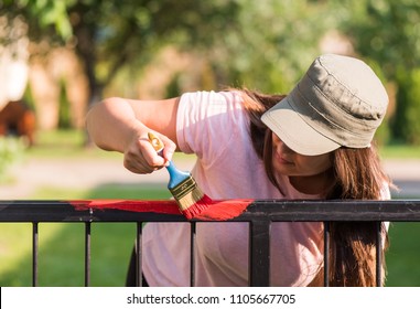 Pretty Girl Is Painting Metal Fence With A Brush