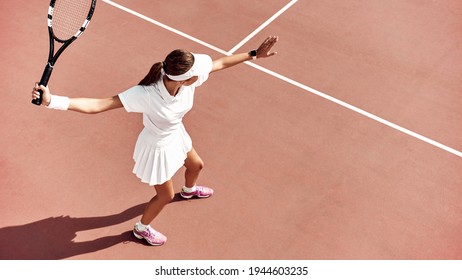 Pretty girl plays tennis on the court outdoors. She prepares to beat on a ball. Woman wears a light blue sportswear with white sneakers. Top view photo. - Powered by Shutterstock