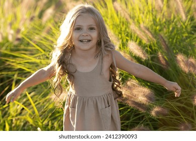 A pretty girl runs across a field with her arms spread wide. A cheerful girl spreads her arms to the sides. Walk outdoors in the city park - Powered by Shutterstock