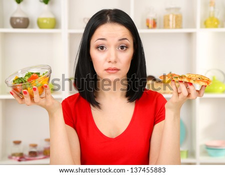 Pretty girl selects pizza or diet on kitchen background