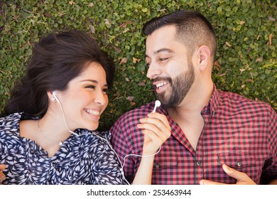 Pretty Girl Sharing Her Earbuds With Her Boyfriend While Relaxing At A Park