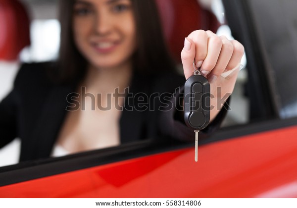 pretty girl sitting in a car and smiling, buying a\
car, red car, keys in\
hand