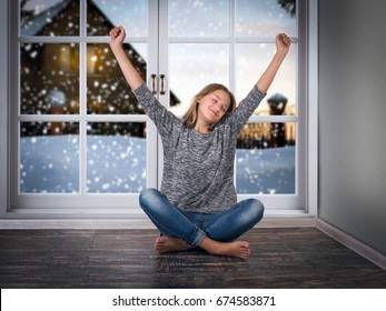 The Pretty Girl Smiles And Pulls His Hands Up While Sitting On The Floor. Large Window. The Snow Outside The Window Of A Village House And Snowdrifts