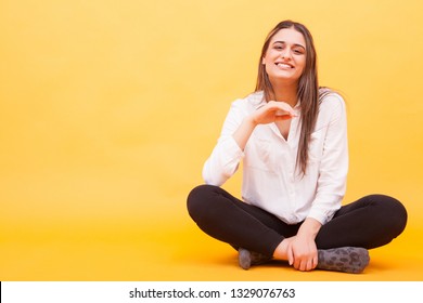 Pretty Girl Smiling At The Camera In Studio And Sitting Down Over Yellow Background. No Worries