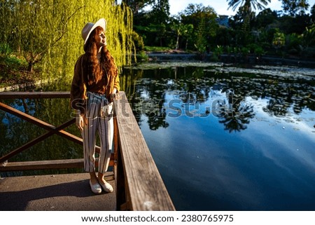 pretty girl standing in front of the lake in mount coot-tha botanic garden, brisbane, queensland, australia; fashionable female model admiring colorful plants at sunset