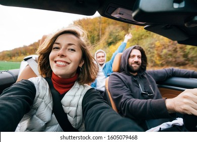 A pretty girl and taking selfie with group of friends during road trip in convertible car. Cheerful millennial students having fun when travel in Europe. - Powered by Shutterstock