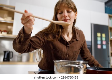 Pretty Girl Tasting Food With Wooden Spoon While Cooking