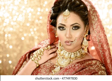 Pretty girl in traditional Indian Pakistani bridal costume with heavy makeup and jewellery against a glittery background