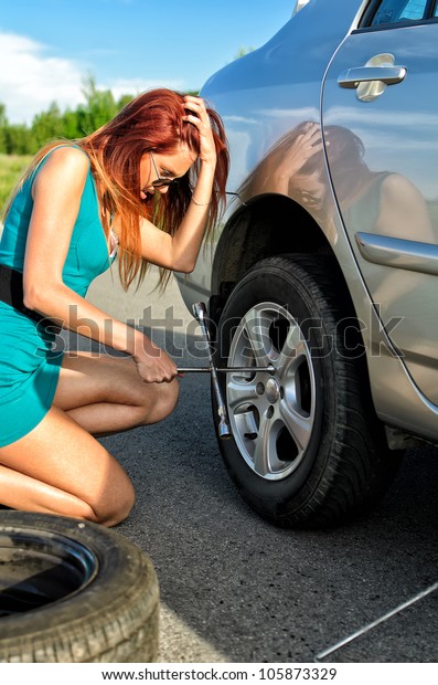 Pretty girl is\
trying to change a tire on a\
road