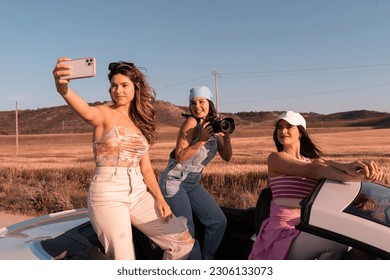 The pretty girl with wavy hair takes a selfie with her two friends as they ride in a convertible car. - Powered by Shutterstock