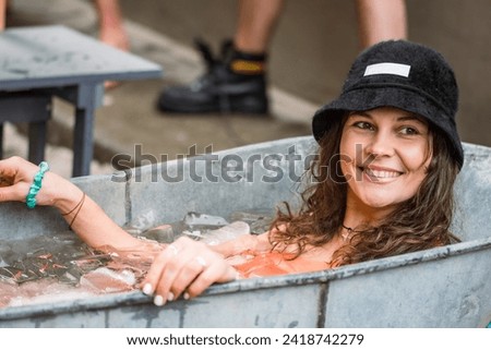 Pretty girl or woman wearing a hat, smiling and ice bathing in the cold water among ice cubes in a vintage bathtub. Wim Hof Method, cold therapy, breathing techniques, yoga and meditation