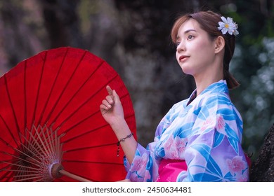 Pretty girl in a Yukata dress. Portrait fashion of Asian women wearing a traditional Japanese kimono or Yukata dress holding a red umbrella with sakura flowers or cherry blossoms blooming in the park. - Powered by Shutterstock