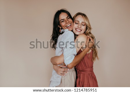 Pretty girls with trendy makeup embracing on light background. Excited caucasian sisters expressing love.