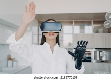 Pretty Handicapped Girl In Virtual Reality Glasses At Home. Disabled Person Gets Rehabilitation And Treatment. Young Caucasian Woman Touches 3d Cyber Vision. Amputee Has Modern Bionic Limb.