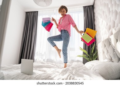 Pretty Happy Woman Having Fun Jumping On Bed At Home With Colorful Shopping Bags On Black Friday Sale Discount Excited