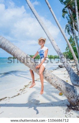 Pretty happy young girl. Smiling and sitting on palm tree at the tropical island beach with clear water.