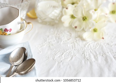 Pretty High Tea Party Table Setting With Cups, Spoons, And Flowers On A Vintage White Cloth With Room Or Space In Center For Copy, Text, Or Your Words.  Horizontal With Short Focus And Blur Background