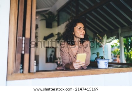 Pretty hipster girl with modern cellphone technology thoughtful looking away thinking about content planning during daytime at terrace, pondering female blogger with digital smartphone gadget
