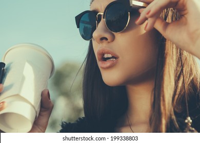 Pretty hipster girl in sunglasses with cup of coffee. Close-up lifestyle outdoor portrait