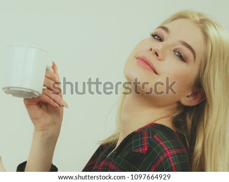 Pretty hipster young adult teenage woman sitting on sofa enjoying her leisure time drinking coffee or tea from mug.