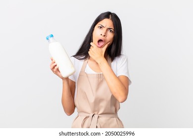 Pretty Hispanic Chef Woman With Mouth And Eyes Wide Open And Hand On Chin And Holding A Milk Bottle