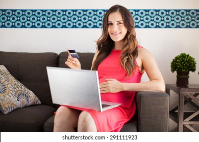 Pretty Hispanic Pregnant Woman Buying Stuff For Her Baby Online With A Credit Card And A Laptop