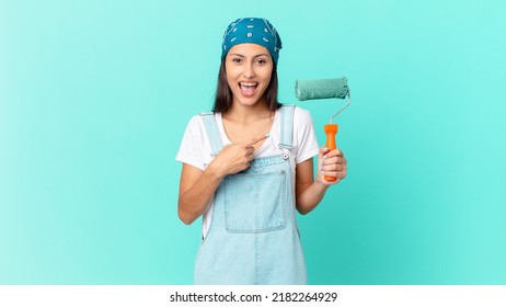 Pretty Hispanic Woman Looking Excited And Surprised Pointing To The Side. Painting Home Concept