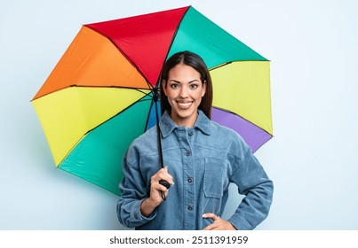 pretty hispanic woman smiling happily with a hand on hip and confident. umbrella concept - Powered by Shutterstock