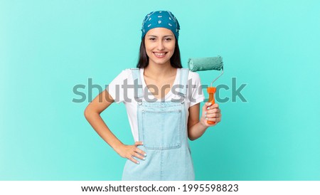 pretty hispanic woman smiling happily with a hand on hip and confident. painting home concept