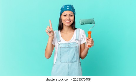 Pretty Hispanic Woman Smiling And Looking Friendly, Showing Number One. Painting Home Concept