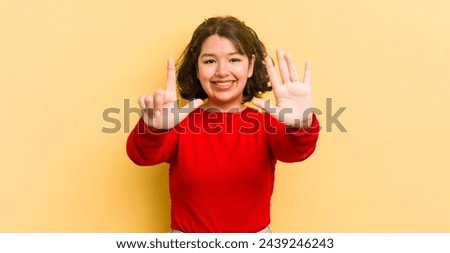 pretty hispanic woman smiling and looking friendly, showing number seven or seventh with hand forward, counting down