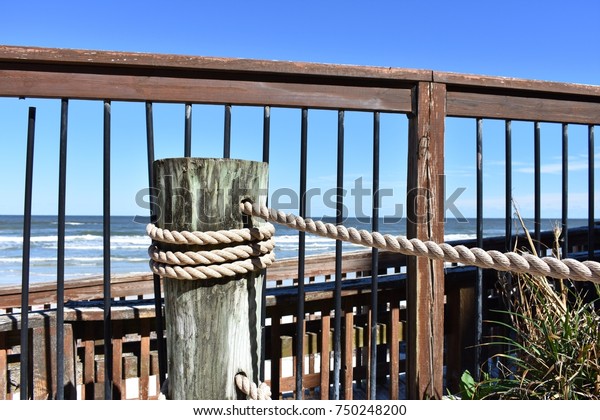 Pretty horizon over water scene\
with wooden railing, ship rope and boardwalk to the\
beach.
