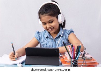 A Pretty Indian Girl Child Attending Online Class With Tablet And Headphone On White Background