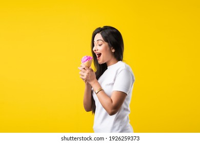 Pretty Indian Girl Or Young Asian Woman Eating Strawberry Ice Cream In Cone Against Yellow Studio Background