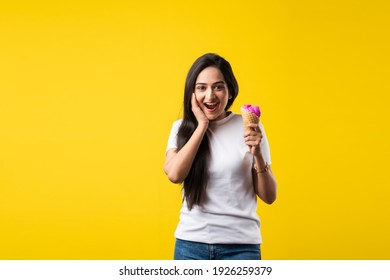 Pretty Indian Girl Or Young Asian Woman Eating Strawberry Ice Cream In Cone Against Yellow Studio Background