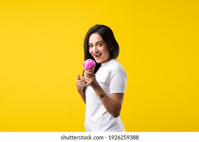 Pretty Indian Girl Or Young Asian Woman Eating Strawberry Ice Cream In Cone Against Yellow Studio Background