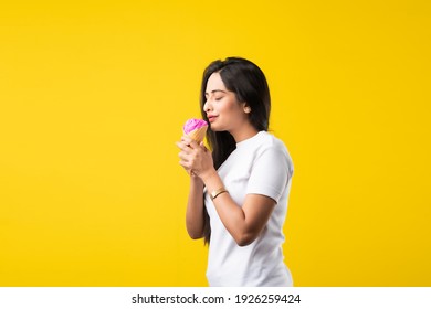 Pretty Indian Girl Or Young Asian Woman Eating Strawberry Ice Cream In Cone Against Yellow Studio Background