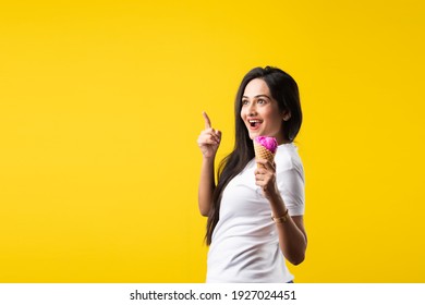 Pretty Indian Girl Or Young Asian Woman Eating Strawberry Ice Cream In Cone Against Yellow Studio Background