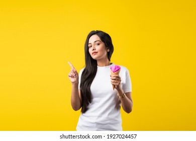 Pretty Indian Girl Or Young Asian Woman Eating Strawberry Ice Cream In Cone Against Yellow Studio Background