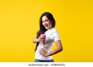 Pretty Indian Girl Or Young Asian Woman Eating Strawberry Ice Cream In Cone Against Yellow Studio Background