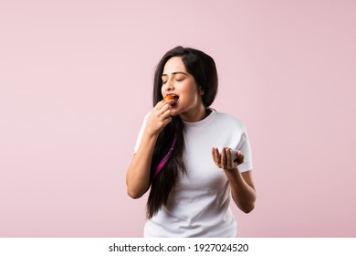 Pretty Indian young girl or woman eating sweet Gulab Jamun against pink background - Shutterstock ID 1927024520