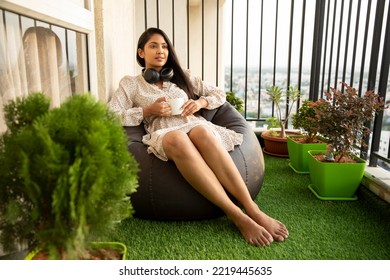 Pretty Indian young woman relaxing with headphone and coffee at balcony. - Powered by Shutterstock