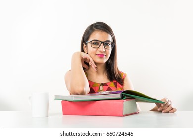 Pretty Indian/Asian collage Girl with spectacles studying on tablet with pile of books