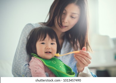 Pretty japanese woman feeding her baby daughter with spoon