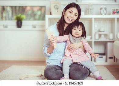 Pretty japanese woman playing with her cute laughing baby girl on the floor at home