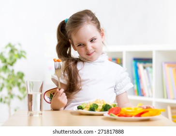 pretty kid girl looking loathingly at healthy vegetables