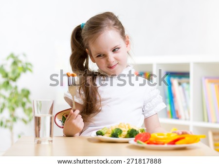 pretty kid girl looking loathingly at healthy vegetables