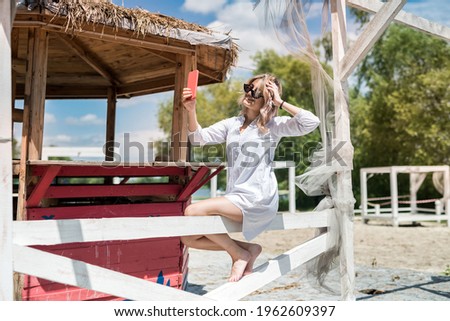 pretty lady holding cell and doing selfie near wooden gazebo at hot summer day. relax and enjot at nature