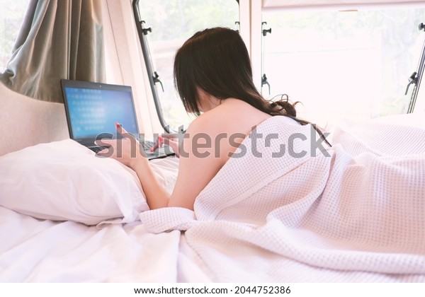 Pretty lady use laptop or notebook on bed in\
caravan, camping car, RV road trip tourist  looking out the window\
of her motorhome. Woman camping in the camper car. assian women\
recreational vehicles.