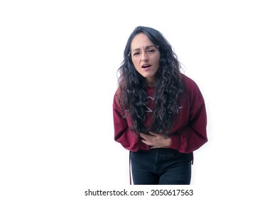 Pretty latin hispanic woman with long thick hair wearing glasses on white background indoors making expressions and gestures, with stomach ache,sick, stressed, hunched over touching her stomach with b
